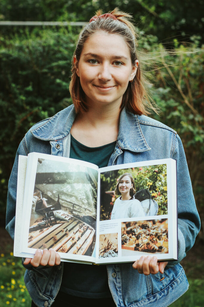 Carolin Lätsch hält ein aufgeschlagenes Buch in die Kamera. Sie lächelt.